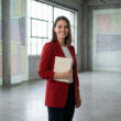 Une jeune femme en blazer rouge tenant un livre dans un espace moderne et épuré.