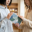 Deux jeunes femmes tiennent ensemble un livre aux motifs de feuilles dans une bibliothèque.